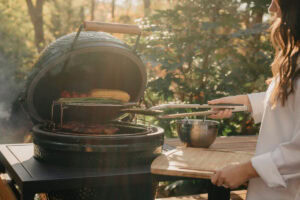 Grilling outdoors with a round smoker grill on a sunny autumn day, woman preparing food in nature.