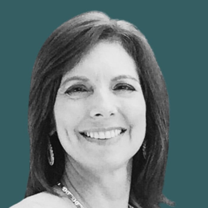 Friendly woman smiling, professional headshot, dark teal background, business attire, outdoor furniture distributor.