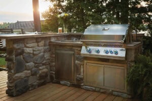 Stainless steel outdoor barbecue grill on stone countertop in a backyard setting, offeredby Napoleon distributer PCS.