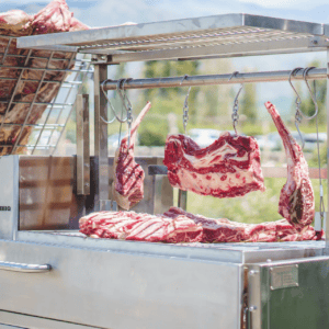 Outdoor grill with hanging and resting meat cuts, stainless steel design.