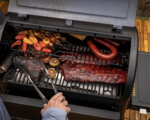 Close-up of a Pit Boss grill with ribs, sausage, and vegetables cooking.