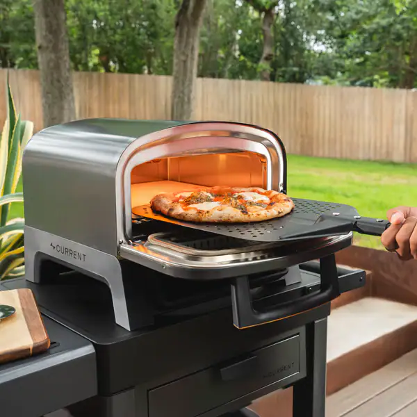 Outdoor pizza oven with a pizza being placed inside by a hand.